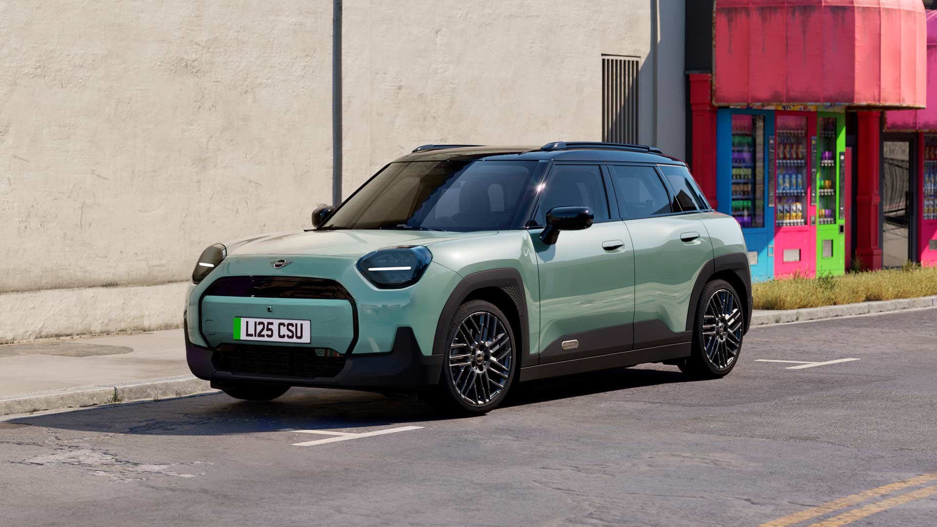 Gray MINI Aceman parked on a city street beside a bright purple and red building, featuring modern design and black roof.
